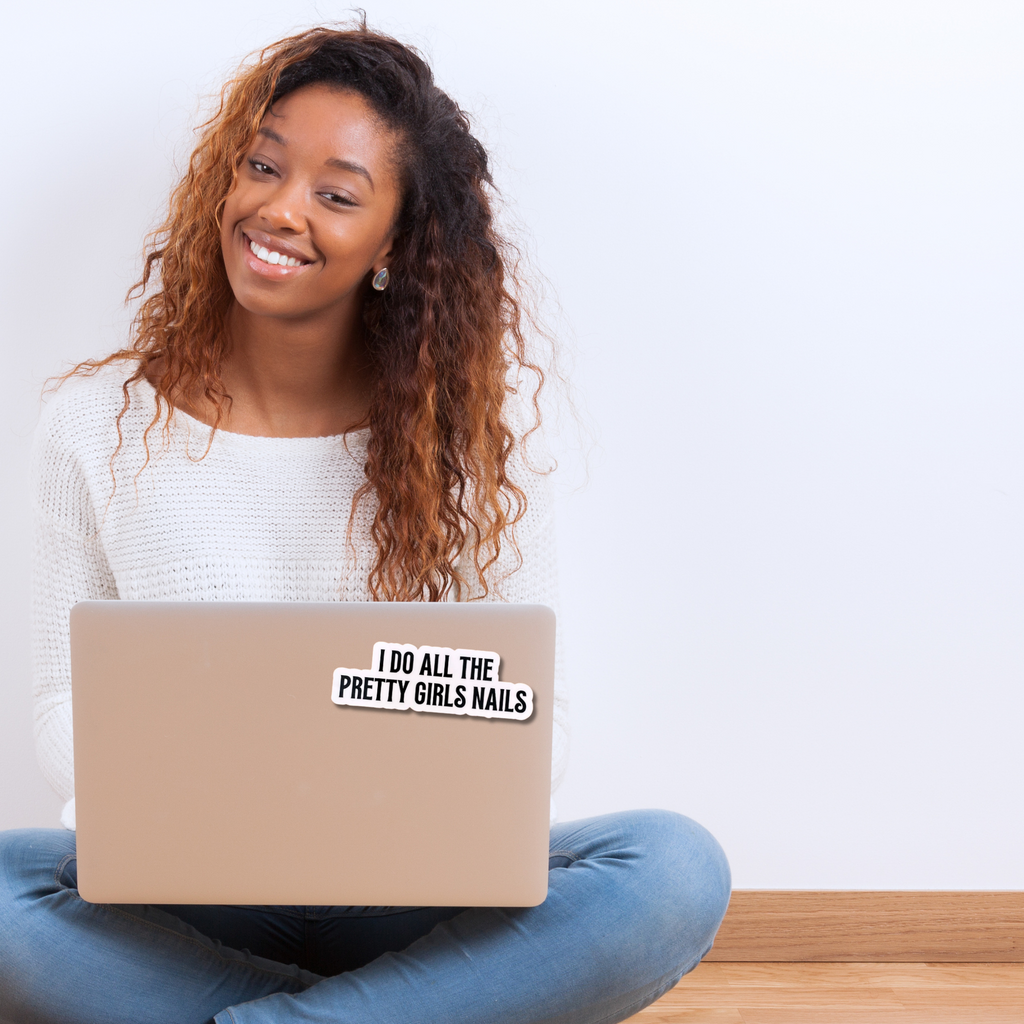Woman sitting on a wooden floor with a laptop featuring a sticker that reads 'I do all the pretty girls nails'.
